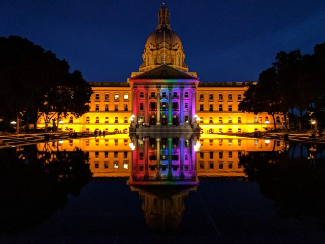 The Alberta Legislature building lit up with Pride colours at night.