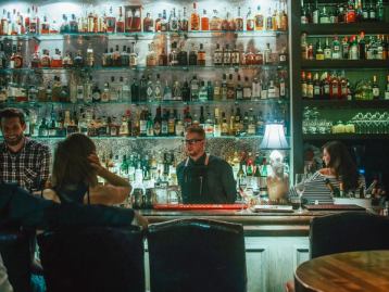 Bartender chatting to seated customer from behind the bar at Proof in Calgary