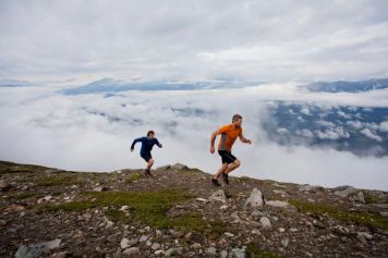 Two men running along a rocky hillside in the Rocky Mountains.