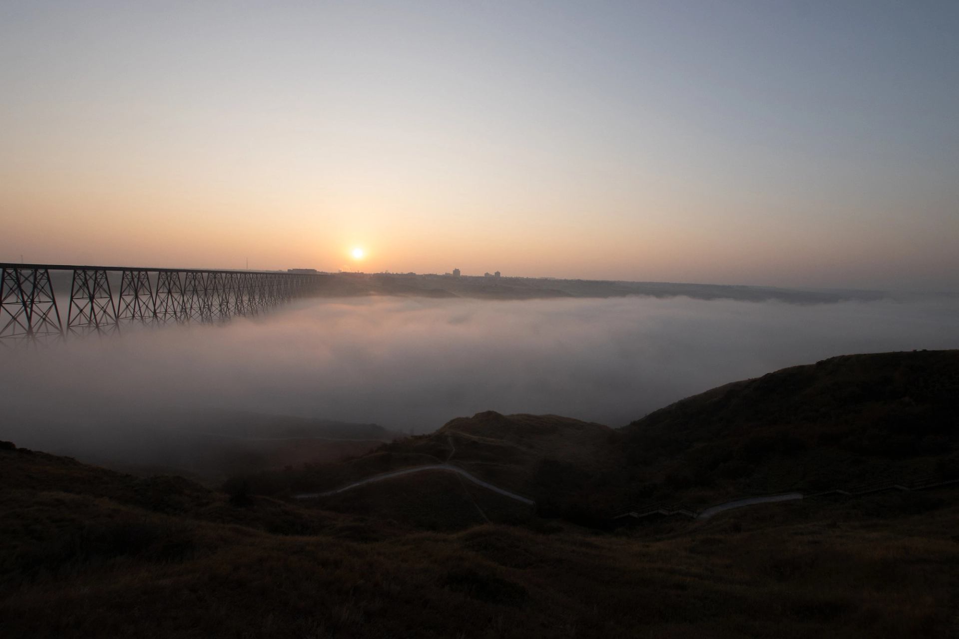 Thick fog rolls through Lethbridge’s coulees near the iconic bridge at sunrise.