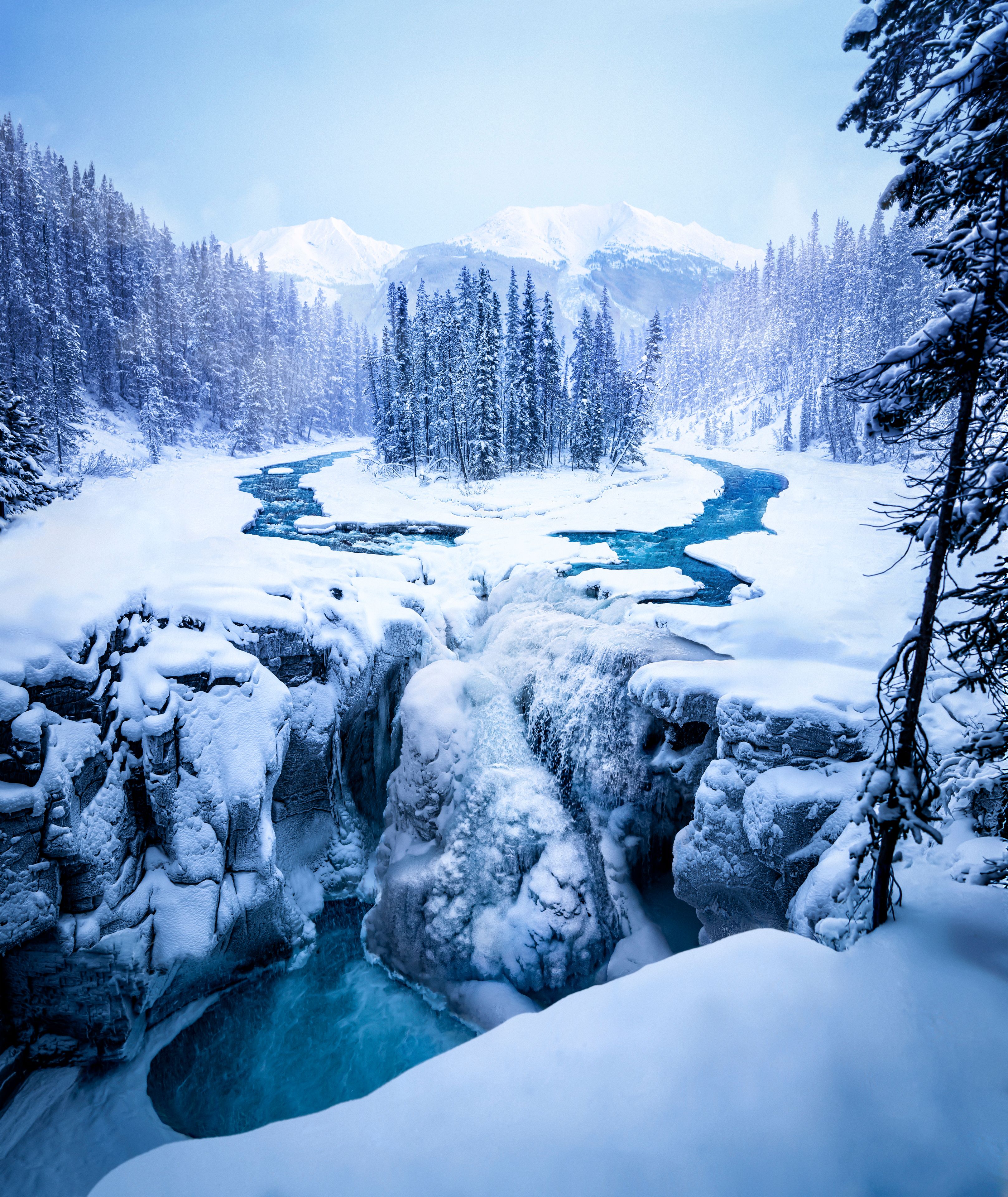 Frost-covered trees surrounded by a freezing river and the start of a waterfall.