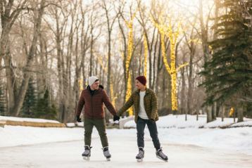 Two men hold hands while ice skating through the lit up trees at Bowness Park in Calgary.