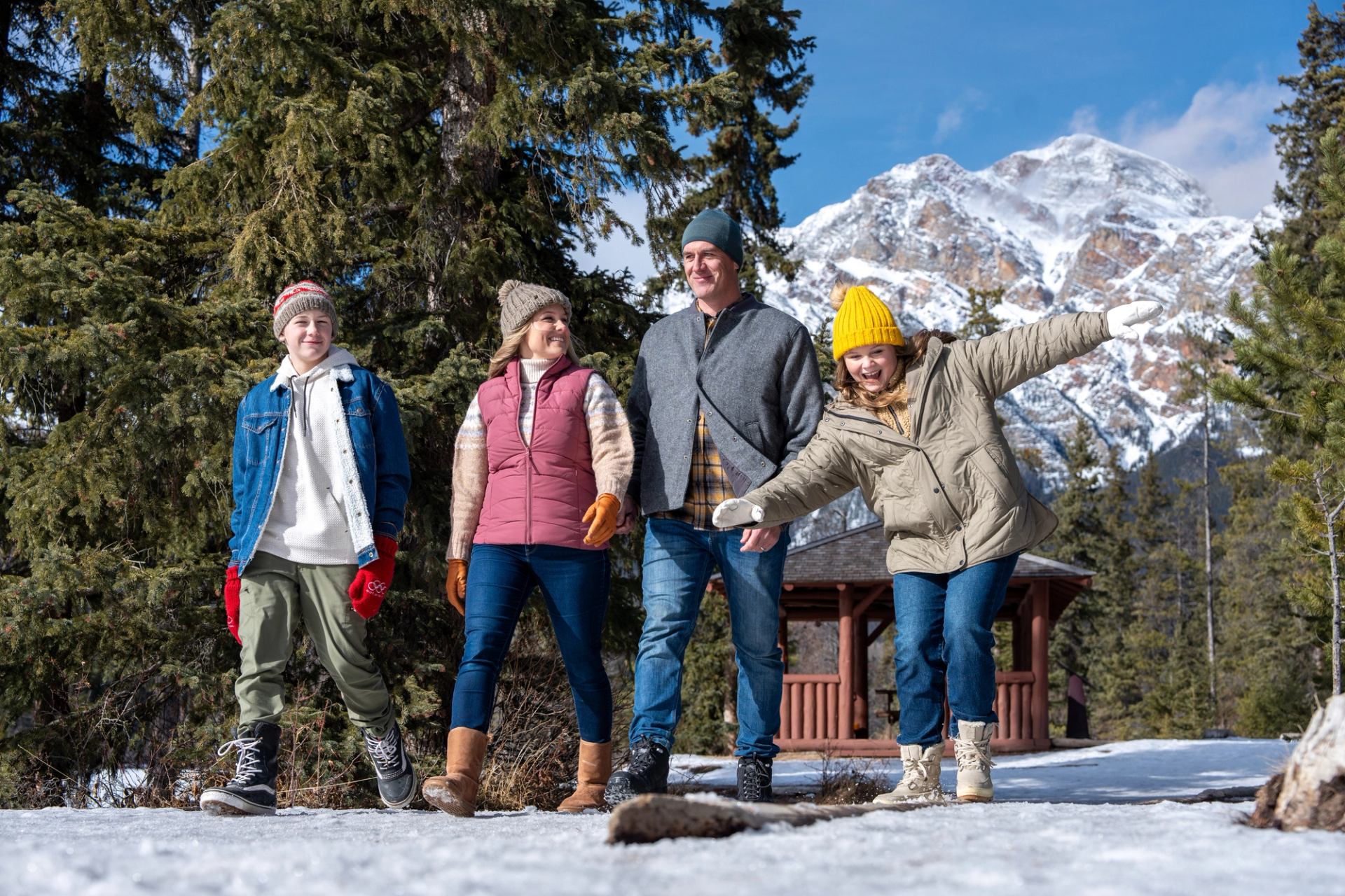A family of four, dressed for cold weather, goes on a winter walk in the Canadian Rockies on a sunny day.