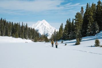 Couple walking through snowy landscape near Mount Engadine Lodge surrounded by mountain scenery.