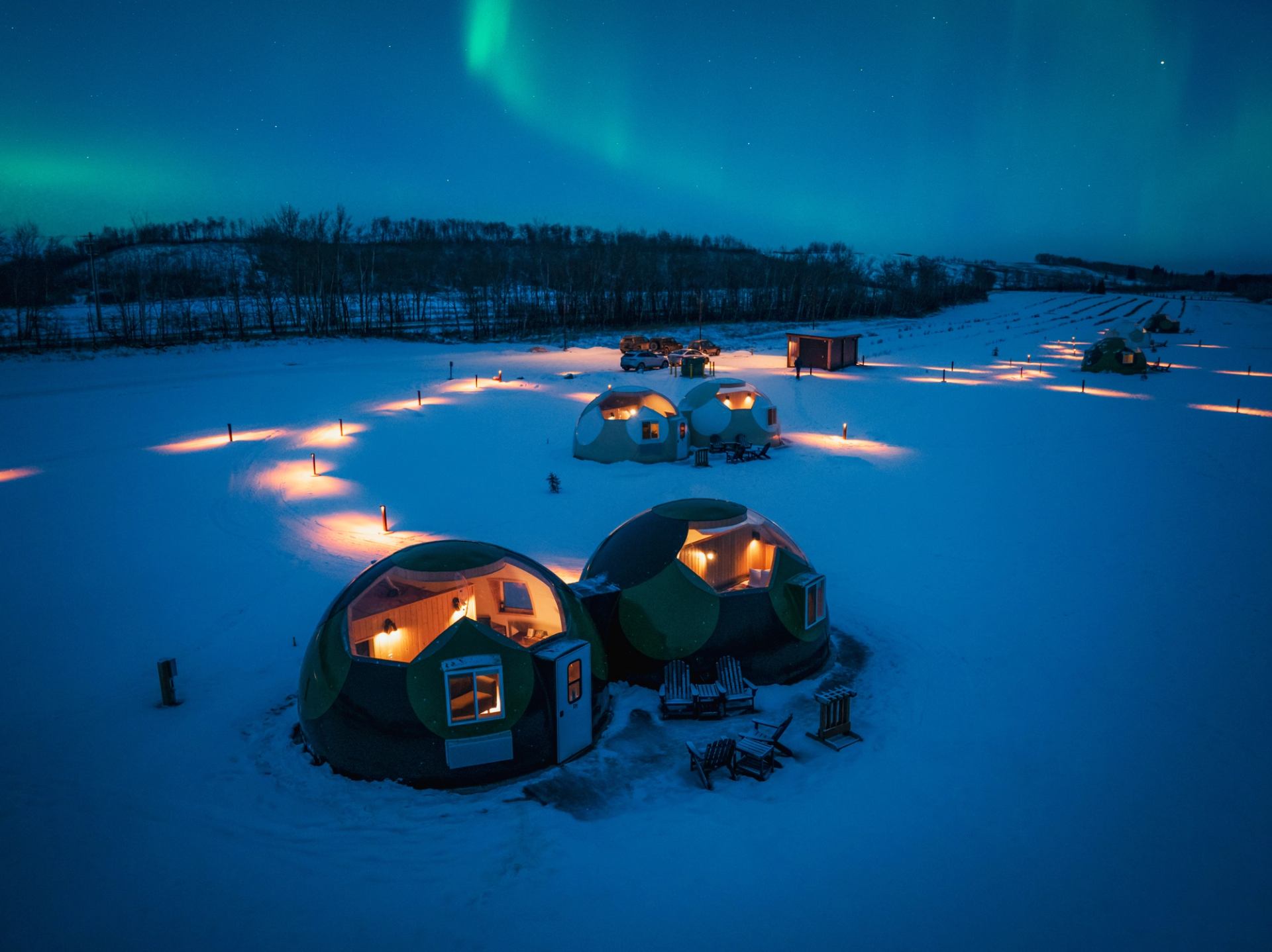 The sky-watching domes at Métis Crossing sit in a snowy landscape under the green northern lights.