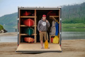 Man with kayaks and paddles on a dock.