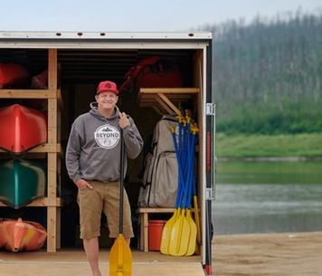 Man with kayaks and paddles on a dock.