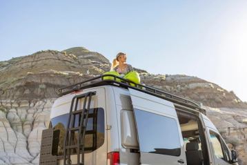 Girl sitting on top of camper van in the Canadian Badlands.