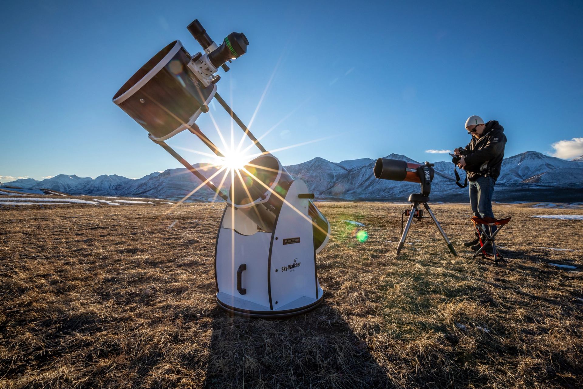 A guide stands by a telescope and other stargazing equipment in a field with mountains in the background.