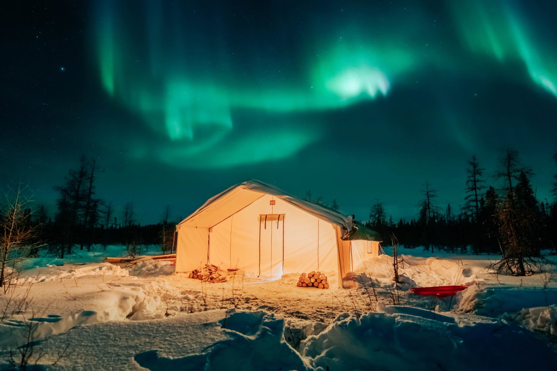 Northern Lights in the night sky above a lighted tent.