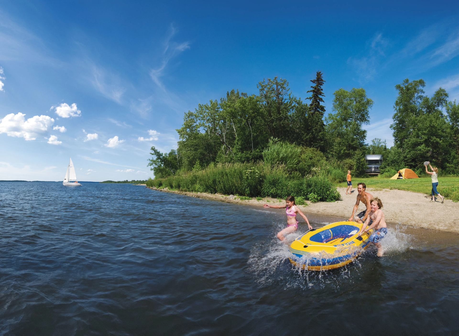 Family having fun, running into a lake with an inflatable with a tent in the distance