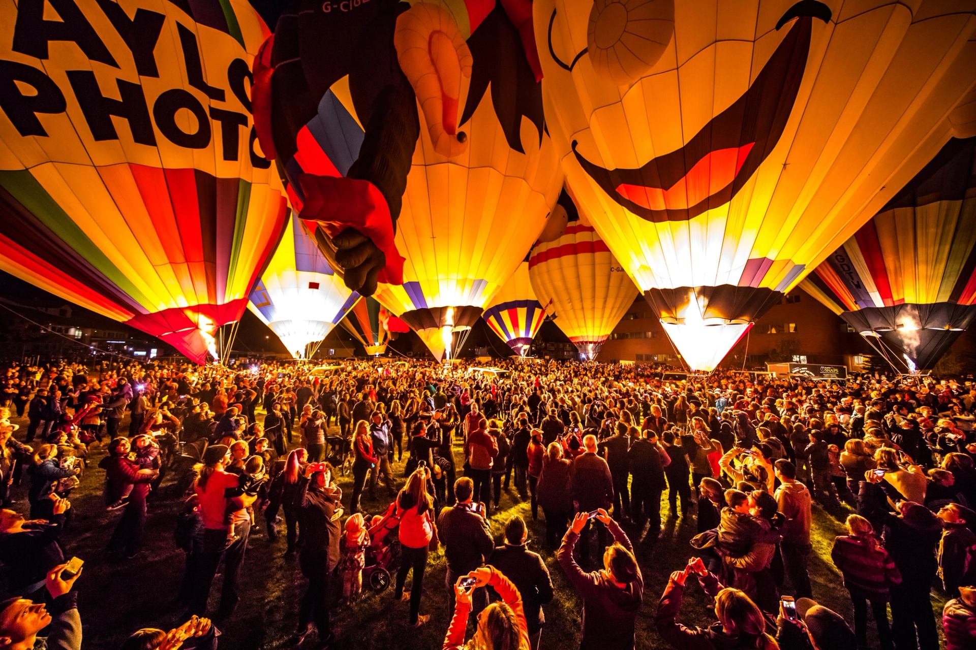 Crowd of people gathered at night to watch hot air balloons take off.