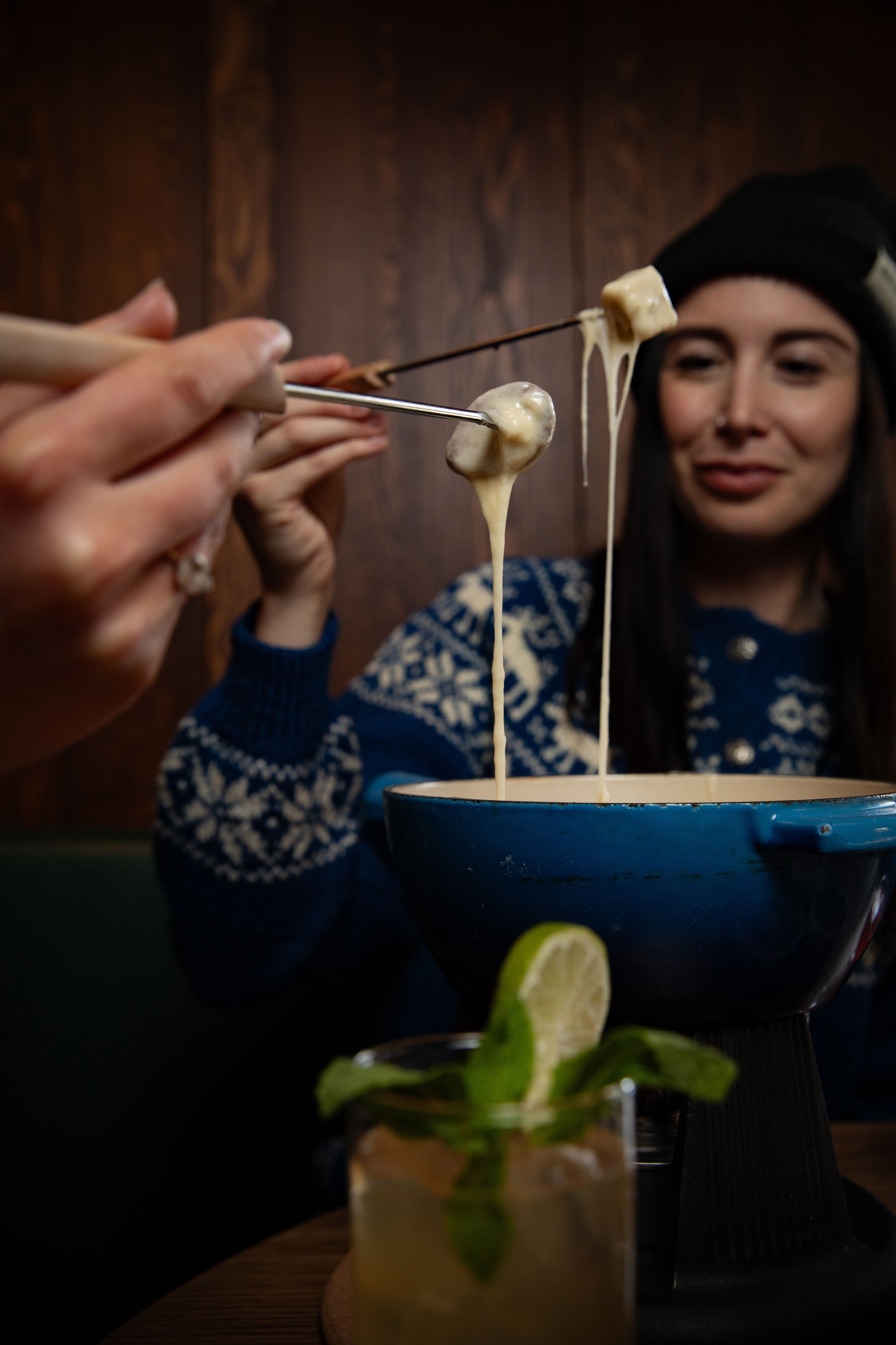 Two diners pull their fondue forks out of a pot of molten cheese at Bluebird in Banff.