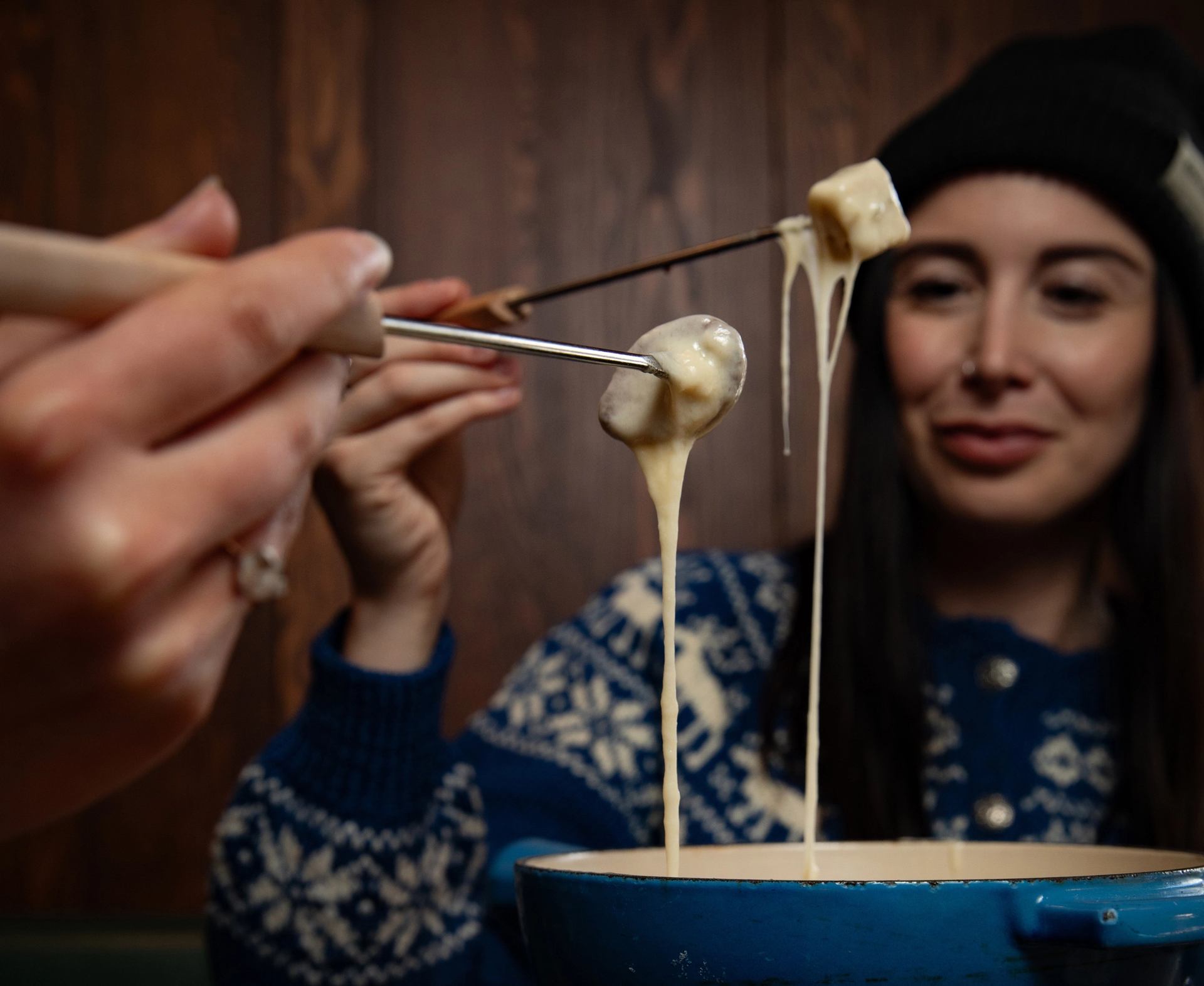Two diners pull their fondue forks out of a pot of molten cheese at Bluebird in Banff.