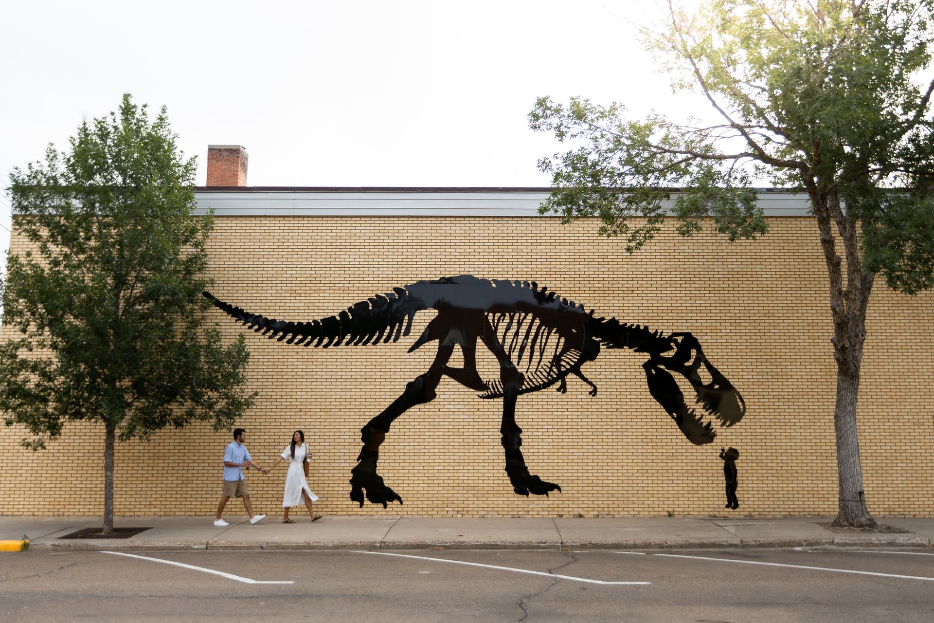 Two people walk past a dinosaur mural in downtown Drumheller.