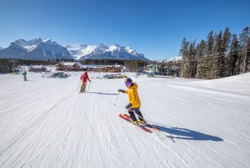 Two skiers, one of them looking back, skiing down a groomed intermediate run at Lake Louise Ski Resort