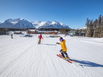 Two skiers, one of them looking back, skiing down a groomed intermediate run at Lake Louise Ski Resort
