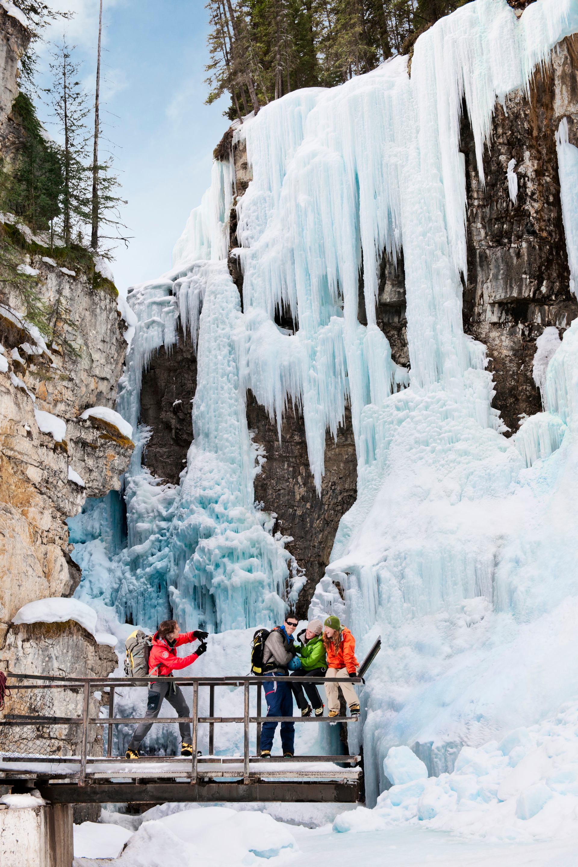 Friends take photos in front of a frozen waterfall while ice walking the catwalks at Johnston Canyon in Banff National Park.