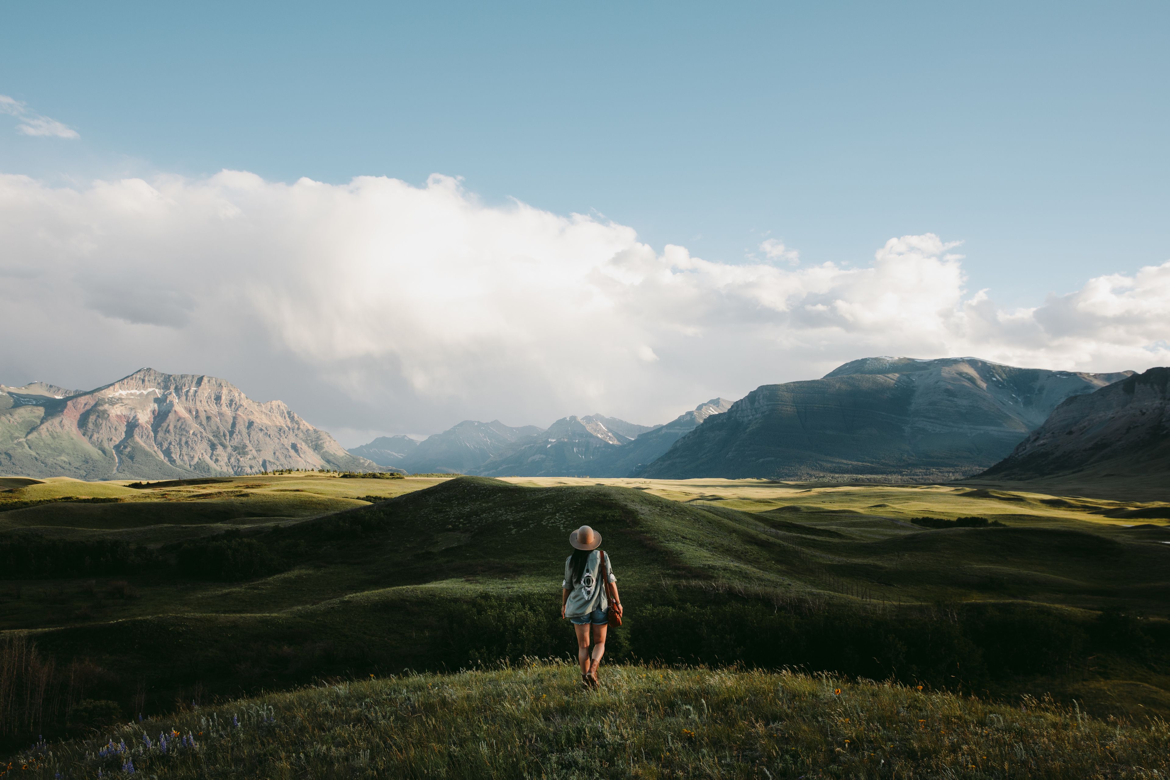 Woman hiking in a meadow towards snow capped mountains in Waterton National Park