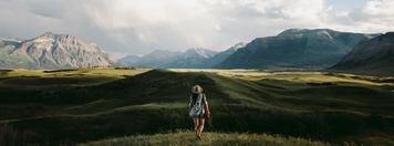 Woman hiking in a meadow towards snow capped mountains in Waterton National Park