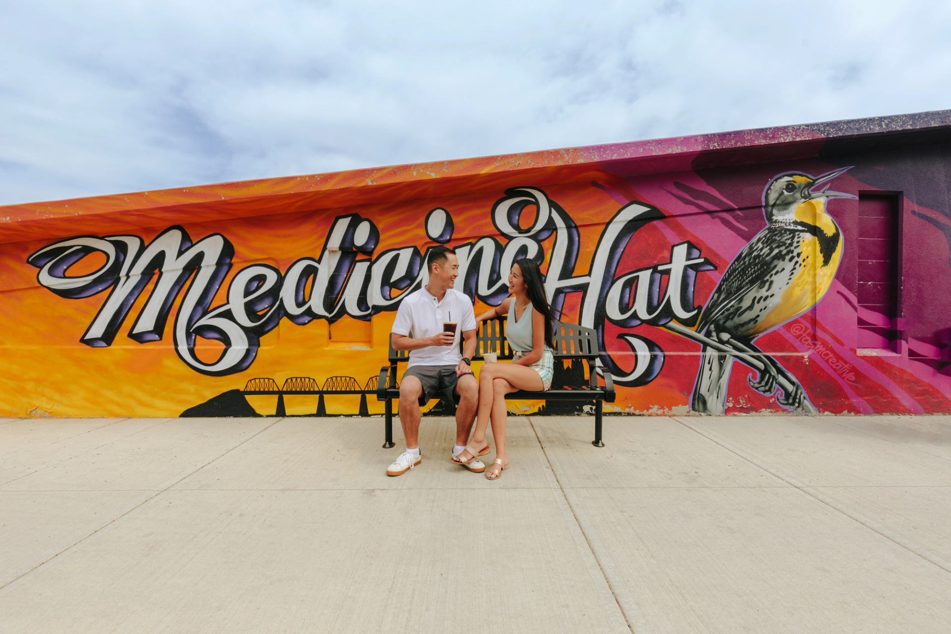 A couple has a coffee in front of the Meadowlark Mural.