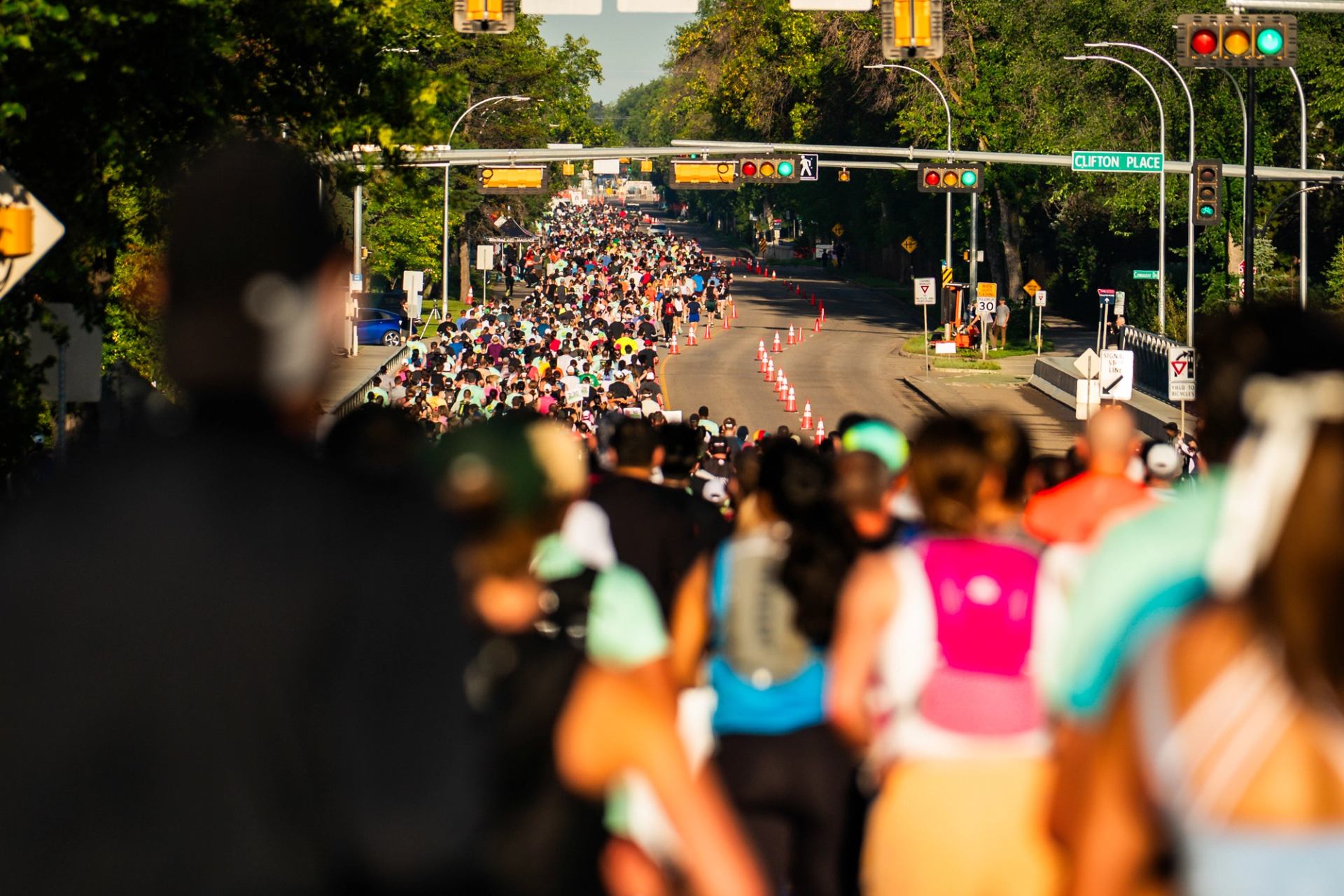 A mass of runners in the Edmonton Marathon run on a tree-lined street.