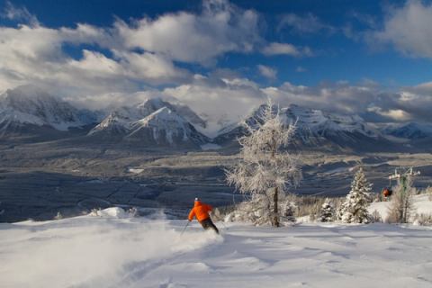 A skier spraying snow behind while skiing a run at Lake Louise Ski resort in Banff National Park.