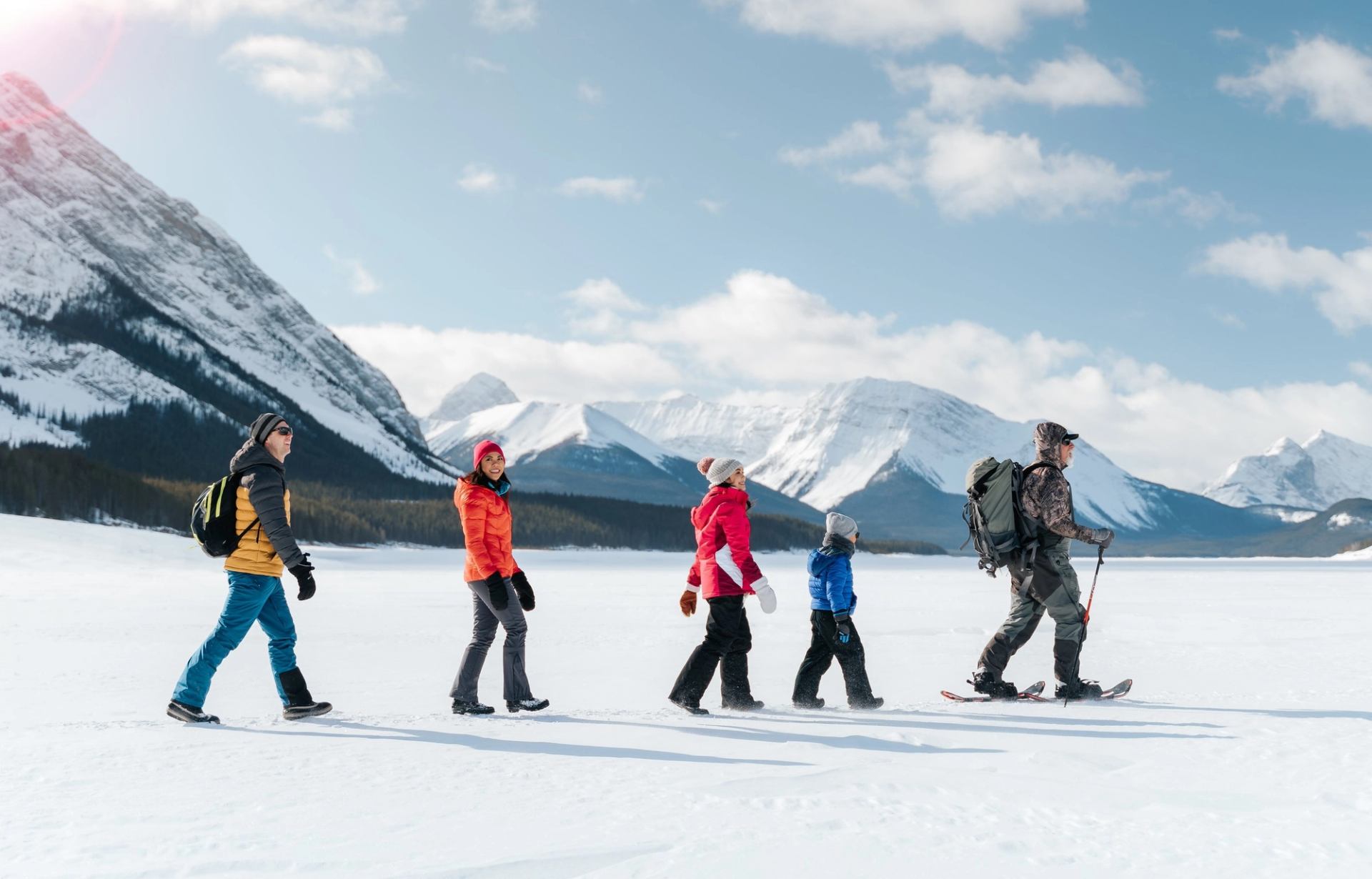 An indigenous An ice fishing guide leads a young family while they trek across the frozen lake looking for an ice fishing spot near Canmore in Kananaskis Country on snowshoes.