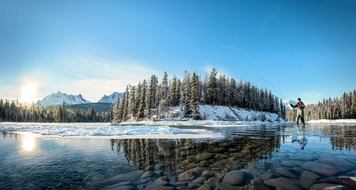 A person fly fishing in the Athabasca River in Jasper National Park.