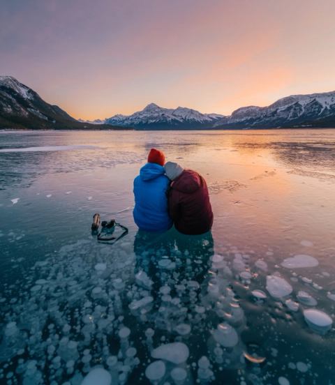 A couple sit on the methane bubbles under a frozen lake while admiring the sunset.