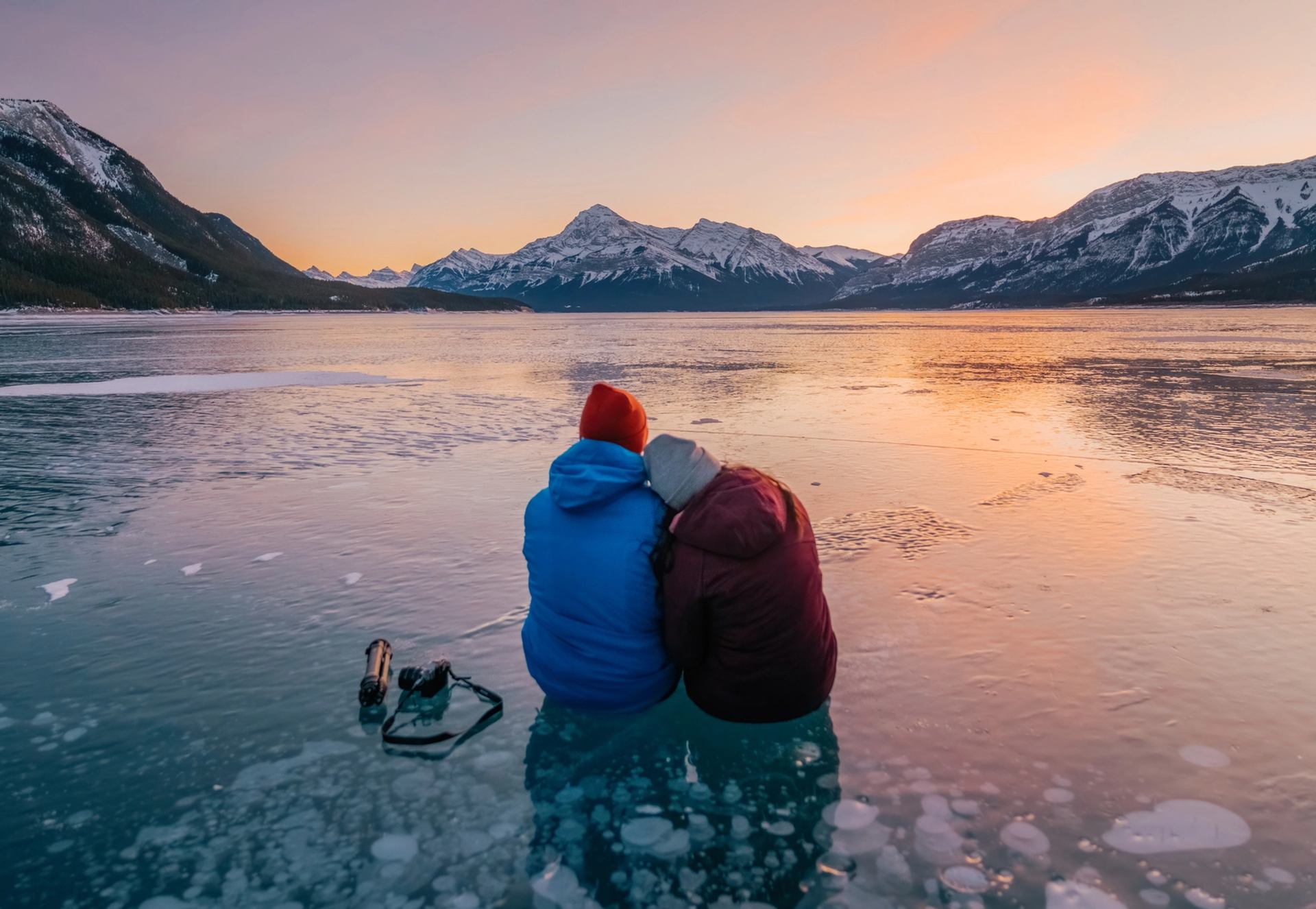 A couple sit on the methane bubbles under a frozen lake while admiring the sunset.
