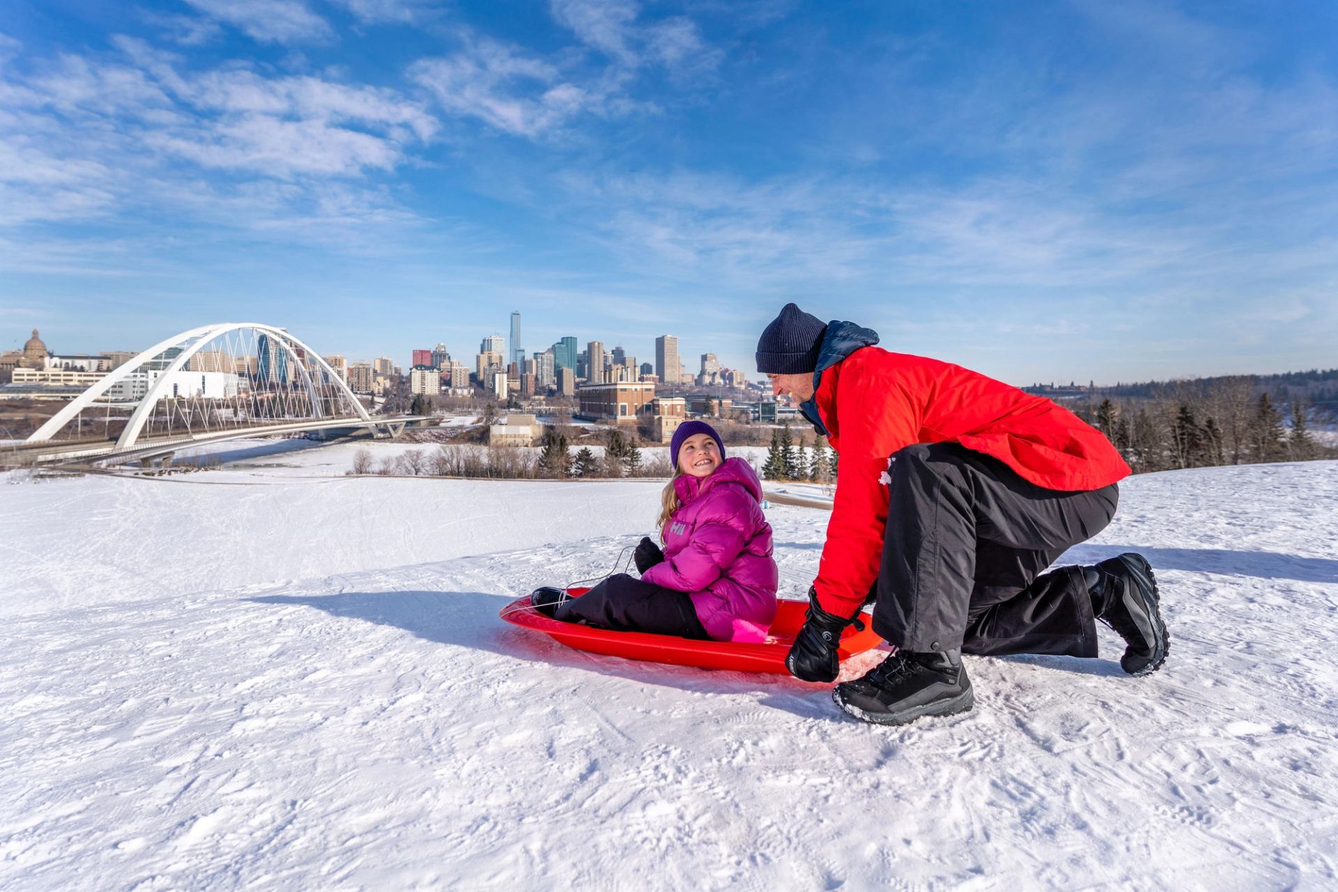 A dad gets ready to push his child down a tobogganing hill at the Indigenous Art Park in Edmonton.