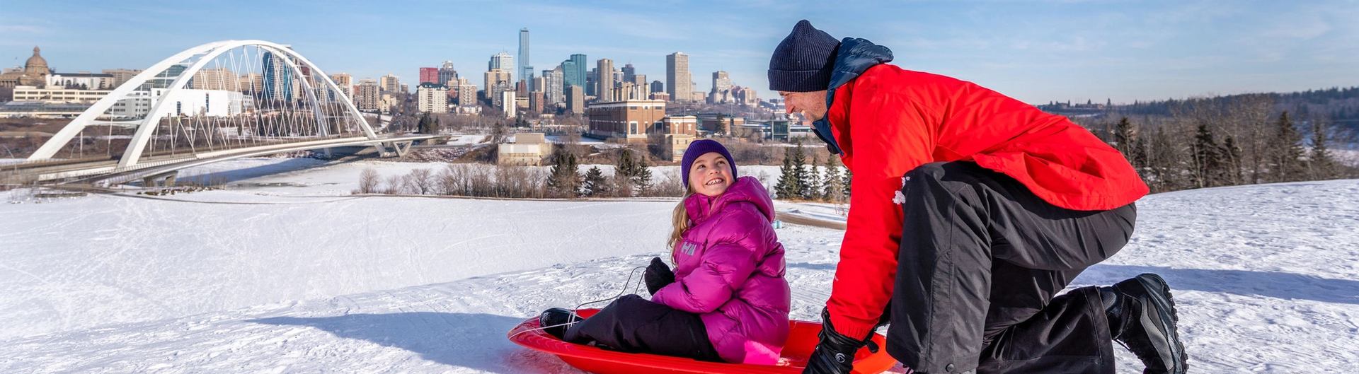 A dad gets ready to push his child down a tobogganing hill at the Indigenous Art Park in Edmonton.