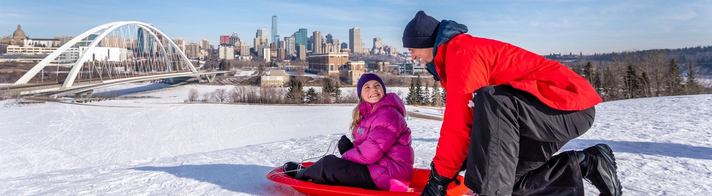 A dad gets ready to push his child down a tobogganing hill at the Indigenous Art Park in Edmonton.
