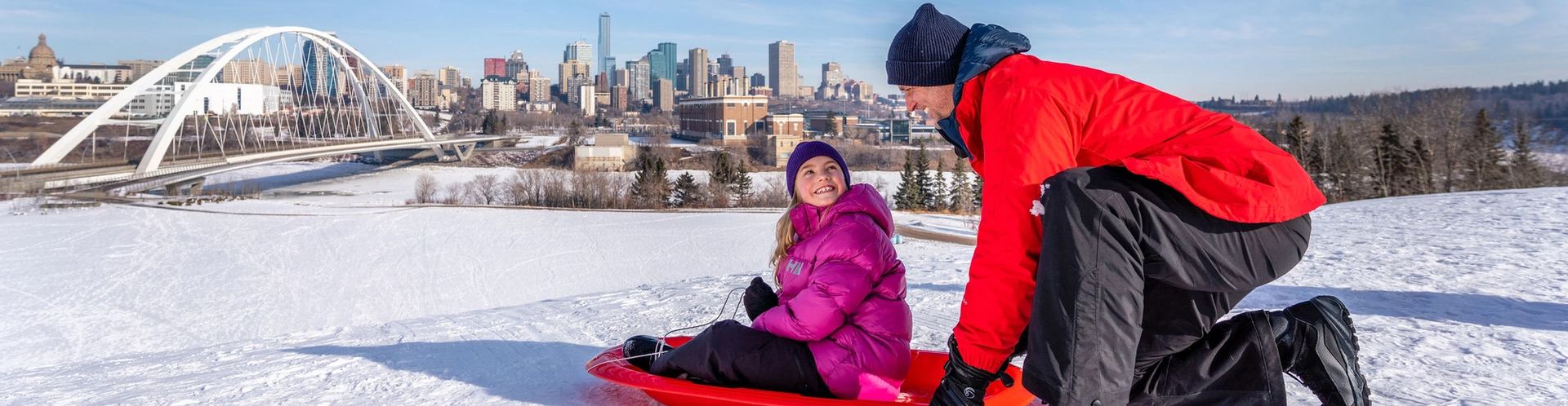A dad gets ready to push his child down a tobogganing hill at Indigenous Art Park in Edmonton.