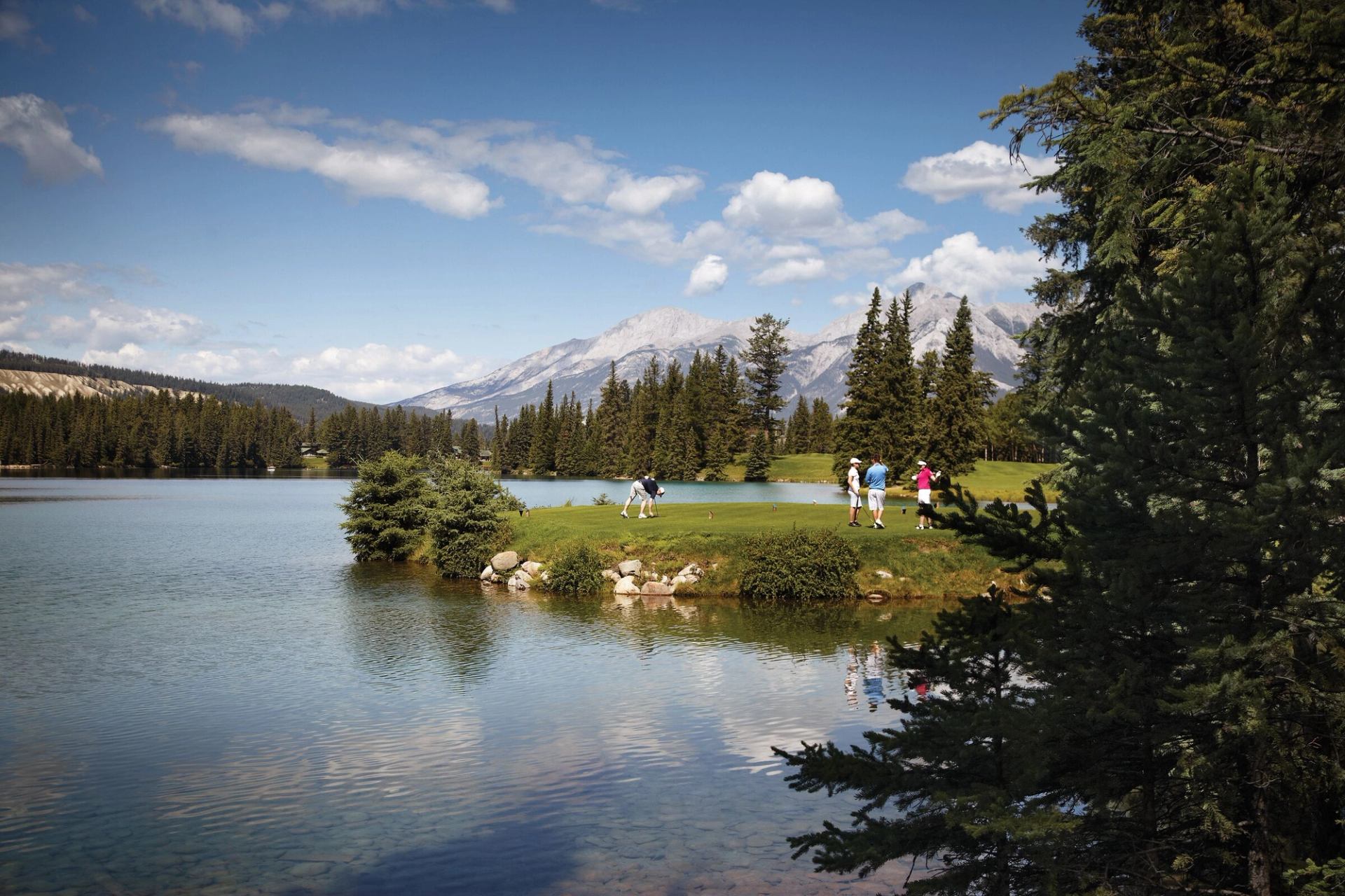 Two golfers walk on a course with a golf cart behind them.