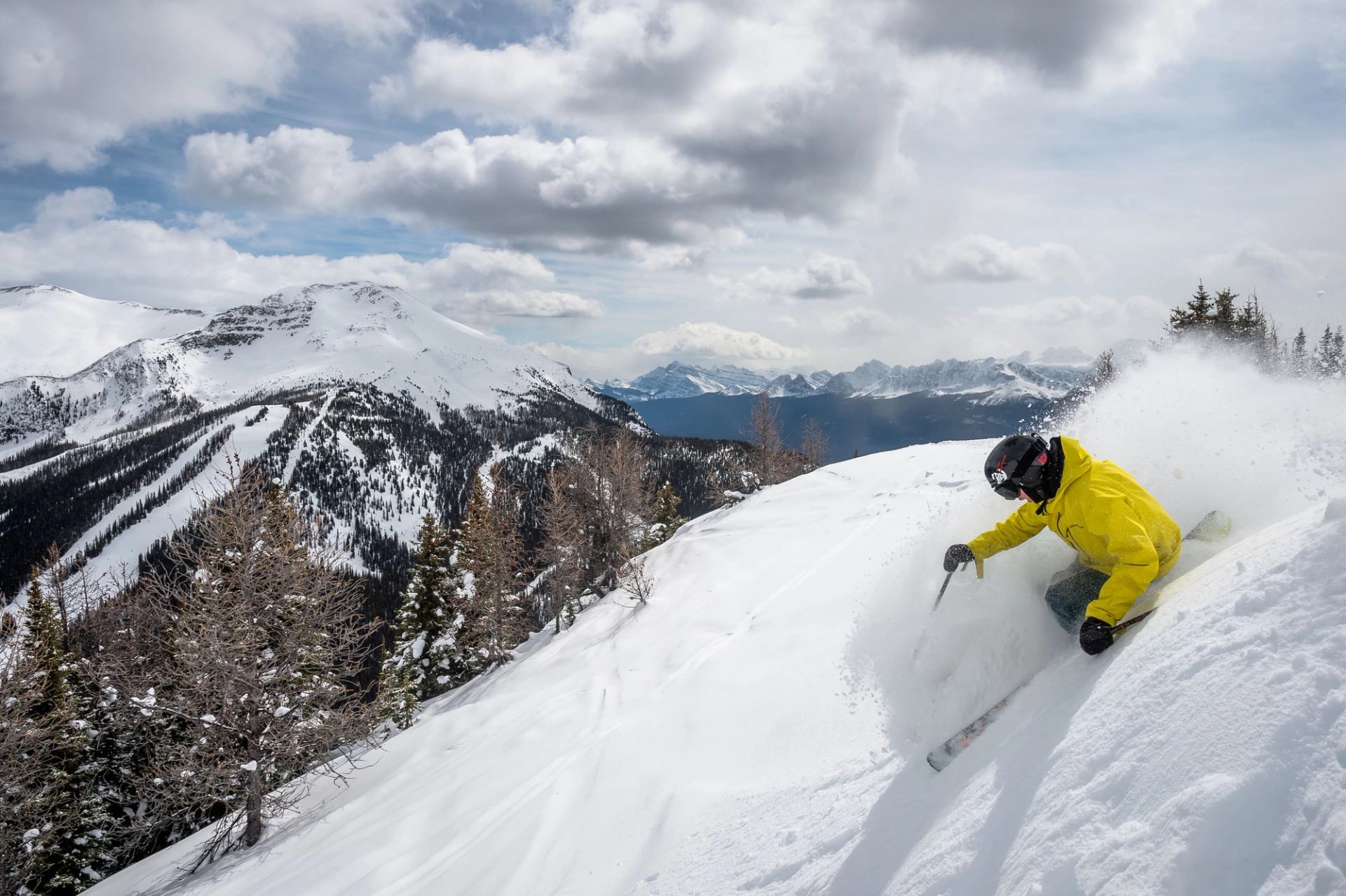 Skier in fresh powder at a steep angle, mountains in the background, skiing at Lake Louise Ski Resort in Banff National Park