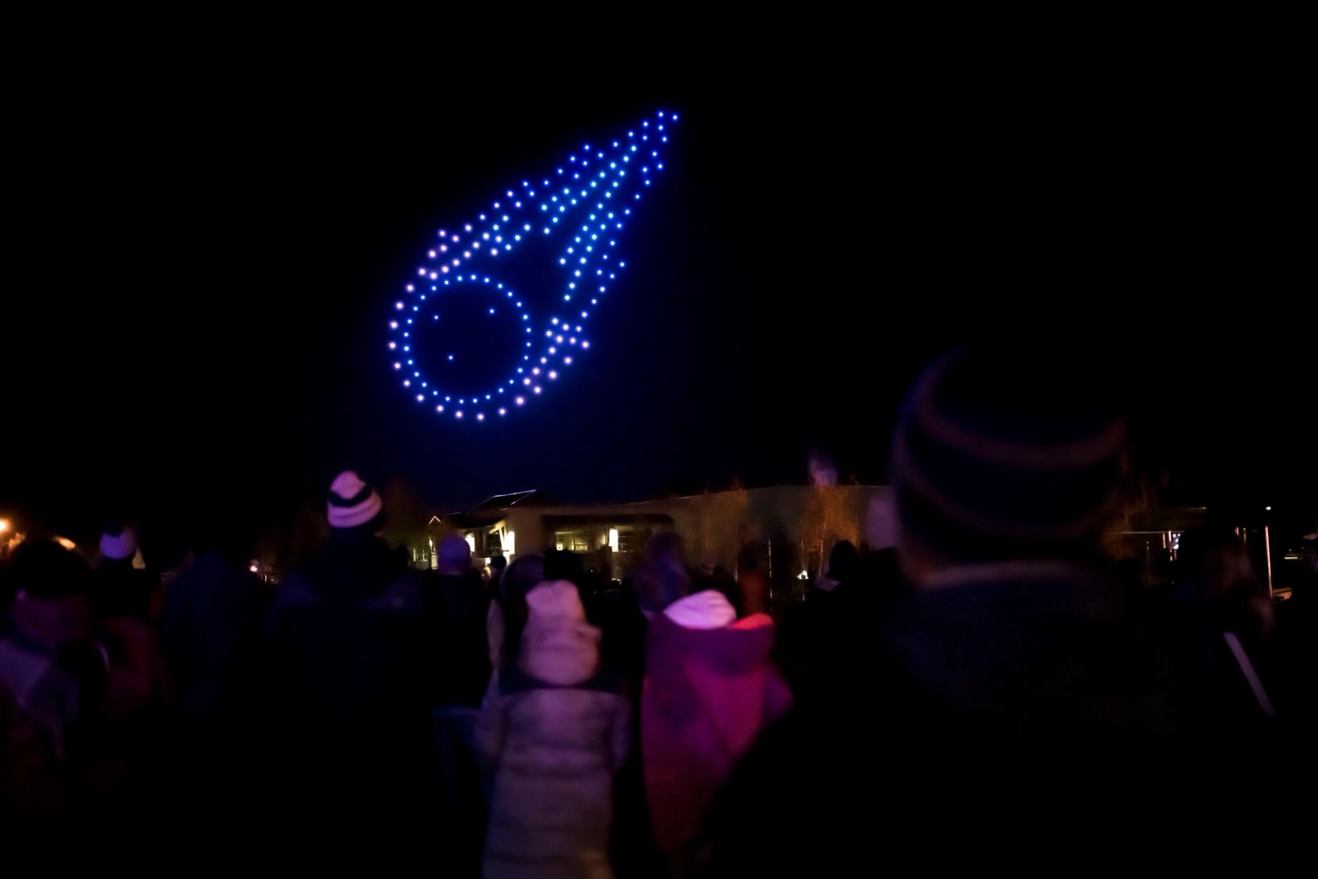 Audience photographed from behind, watching drone show