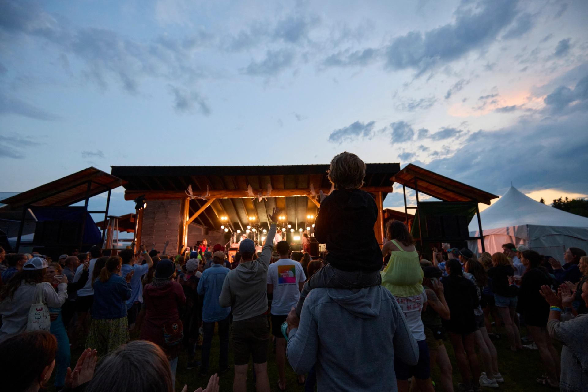 A crowd watching a band playing music, one man has a child on his shoulders