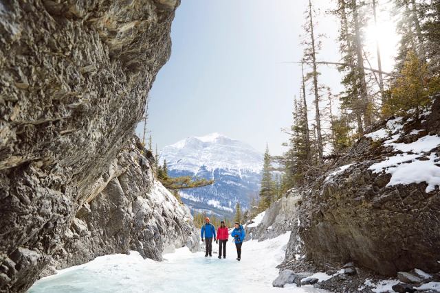People ice walking and winter hiking through Grotto Canyon with mountain views in the background, near Canmore in Kananaskis Country