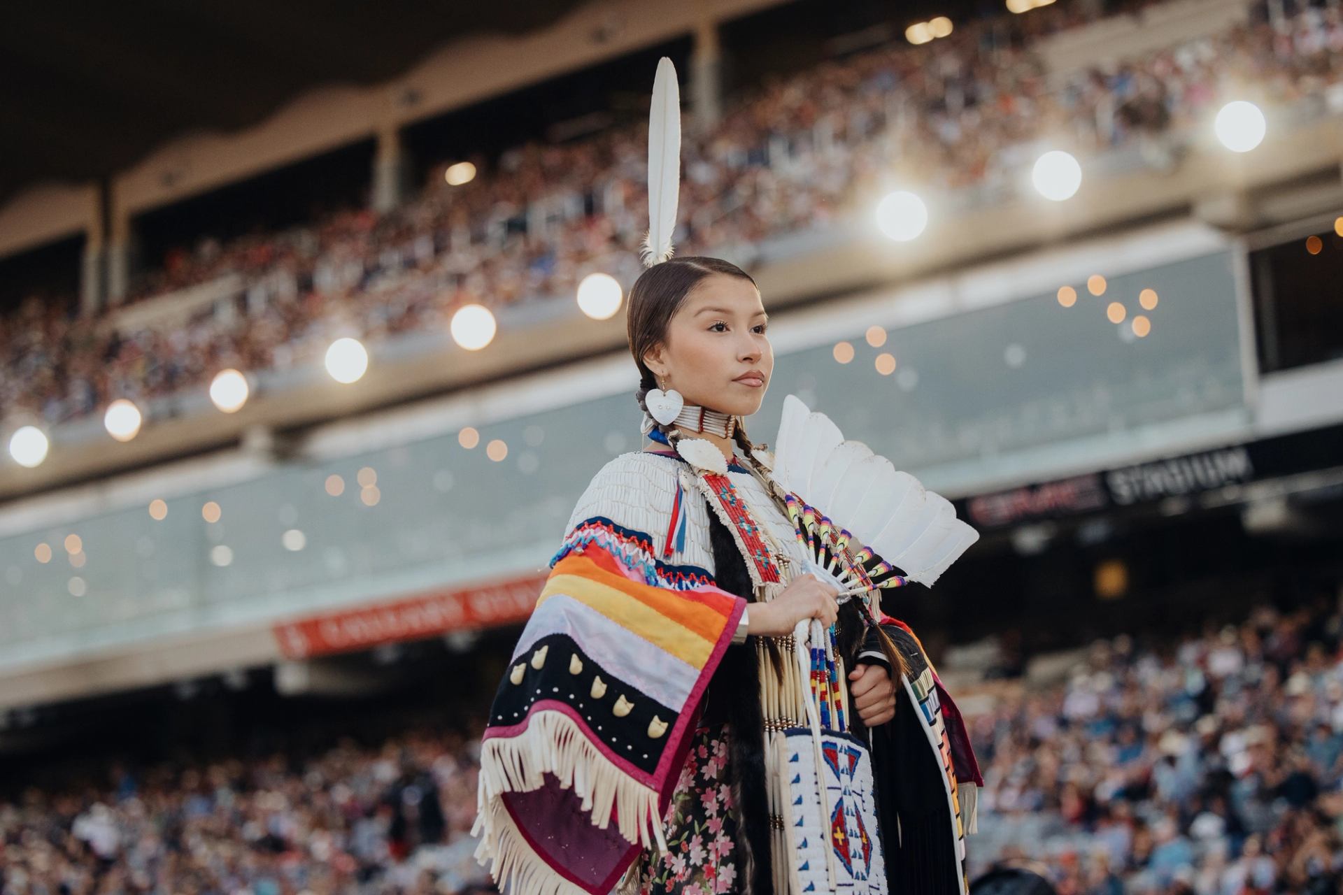 Female Indigenous performer standing in front of a large stadium crowd.