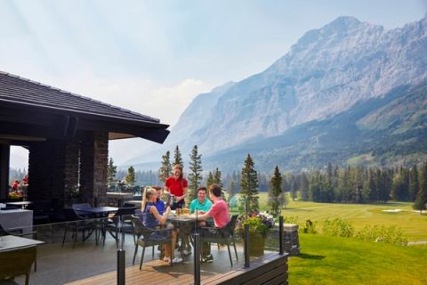 A group of people dine on a patio at a golf clubhouse in the mountains.