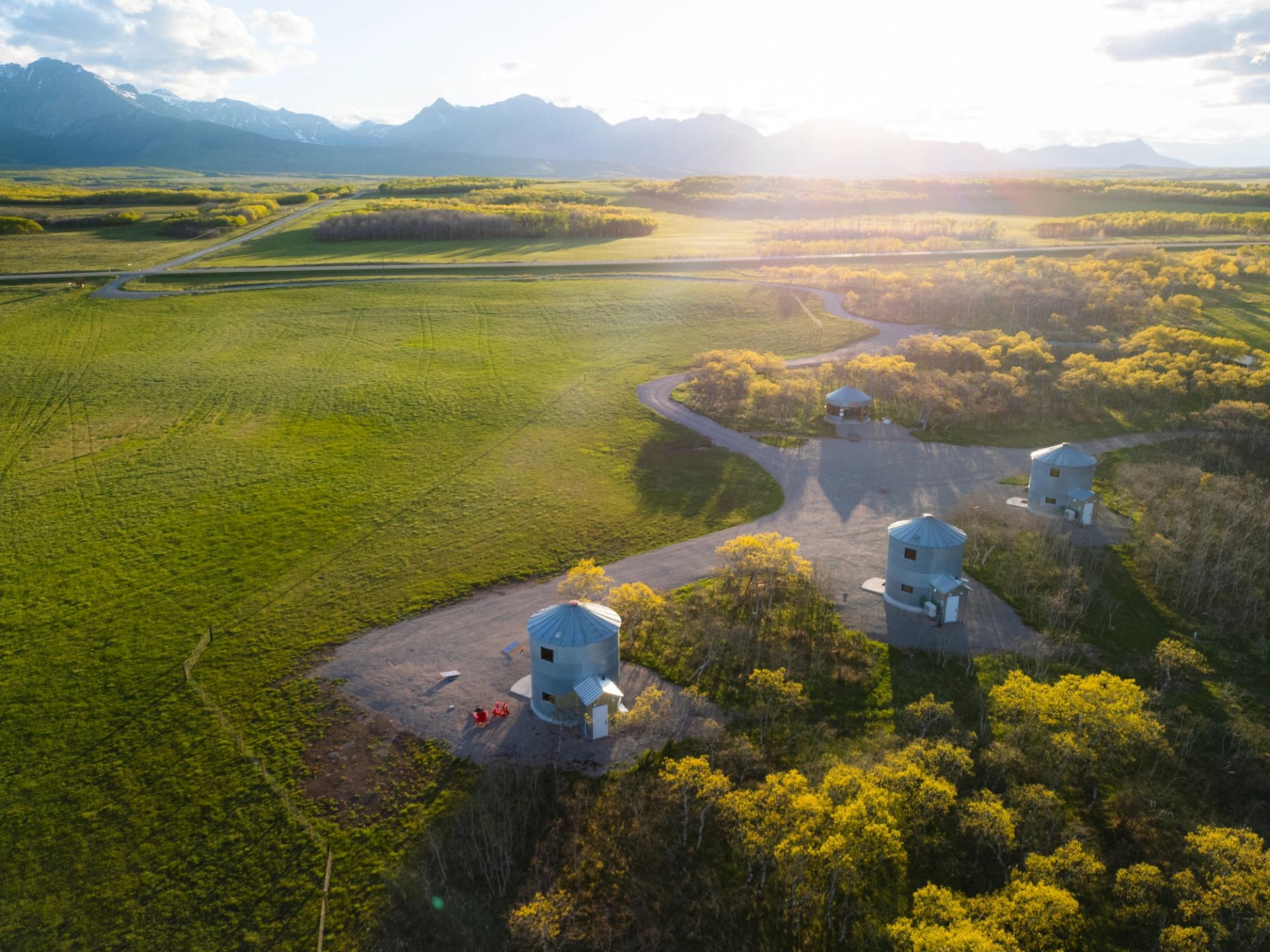 An aerial view of Twin Butte Silos in a green field, with the Canadian Rockies in the distance.