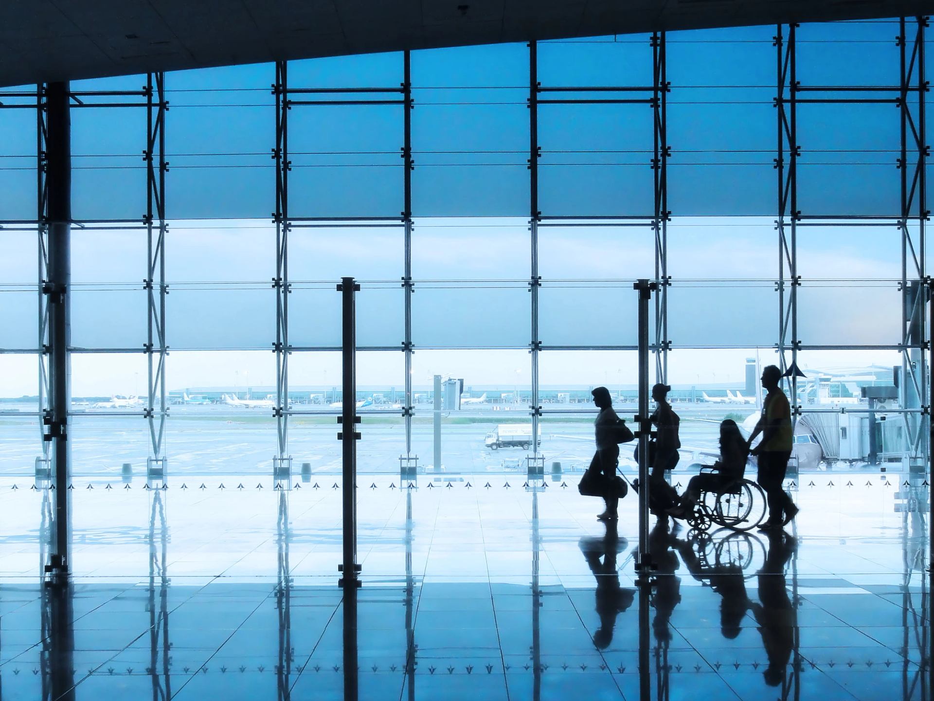 A silhouette of a group moving through an airport, including a person in a wheelchair.