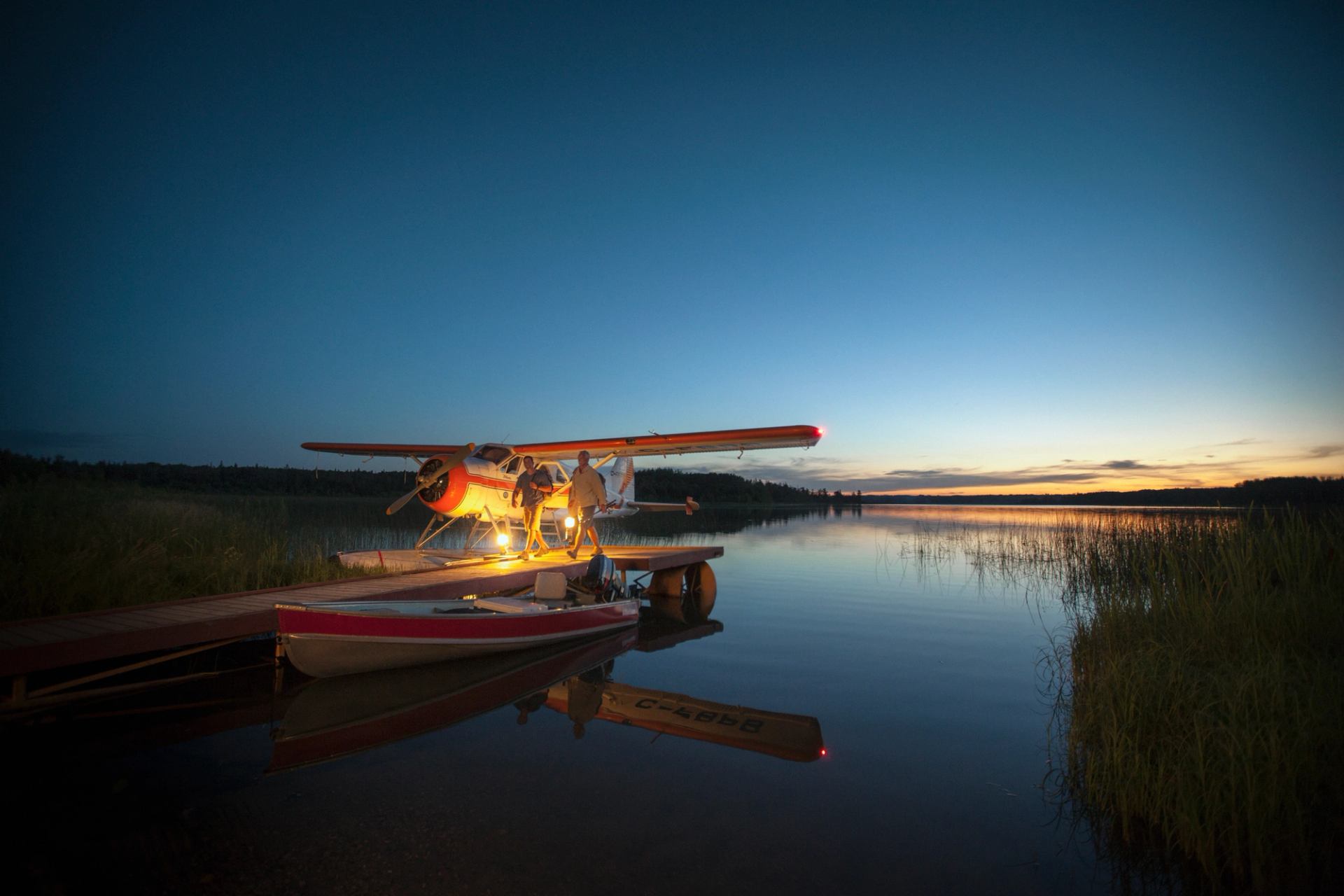 People walking on dock at sunset with float plane and boat attached to the dock