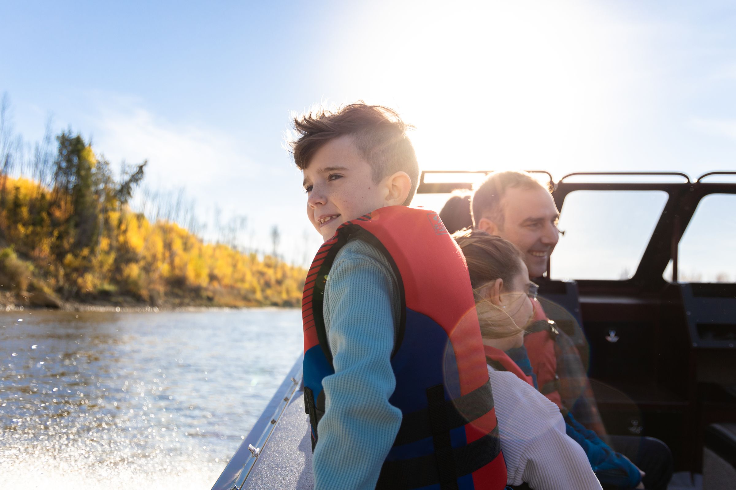 Little boy leaning on side of boat, family behind on the boat in Fort McMurray