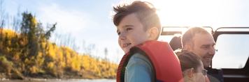 Little boy leaning on side of boat, family behind on the boat in Fort McMurray