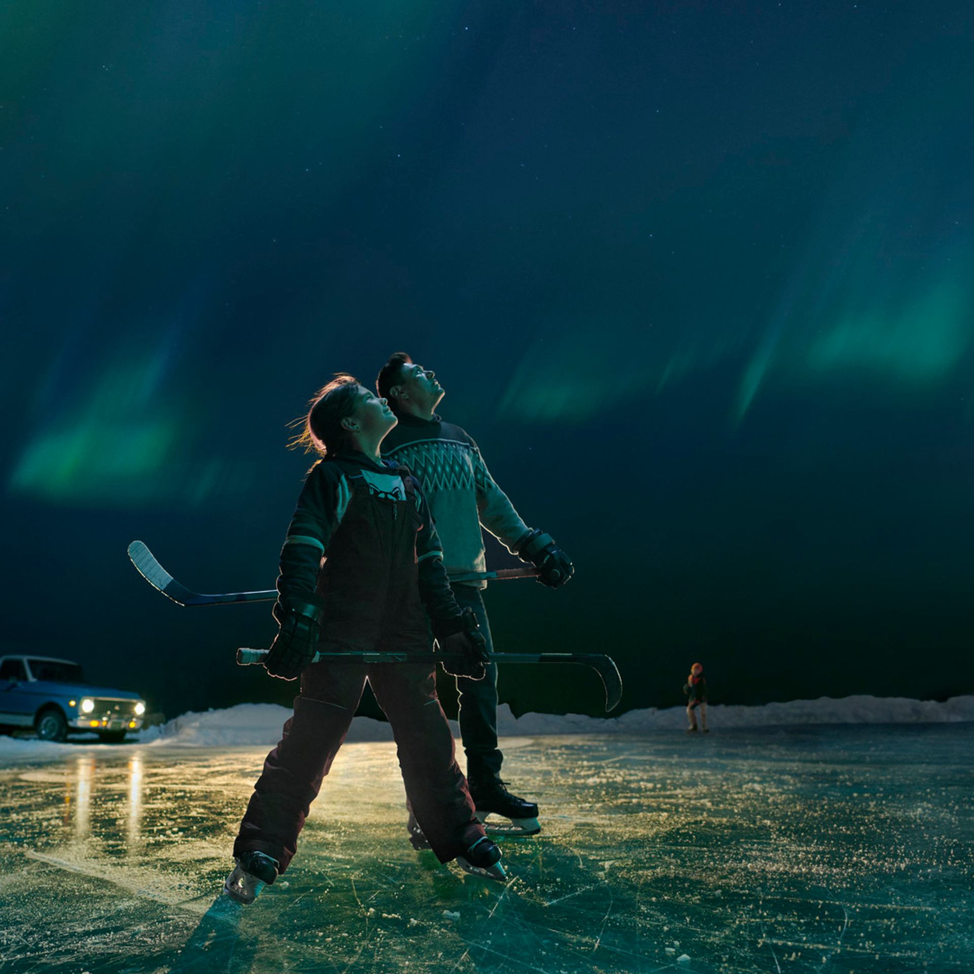 Hockey coach and player pausing from playing pond hockey to look up and admire the Northern Lights overhead.