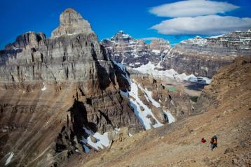 Wide shot of people hiking across rocks on a mountain with multiple mountain peaks in the background