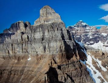 Wide shot of people hiking across rocks on a mountain with multiple mountain peaks in the background